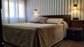 A neatly made bed with patterned bedding, a bedside table with a lamp, and a wall-mounted clock.