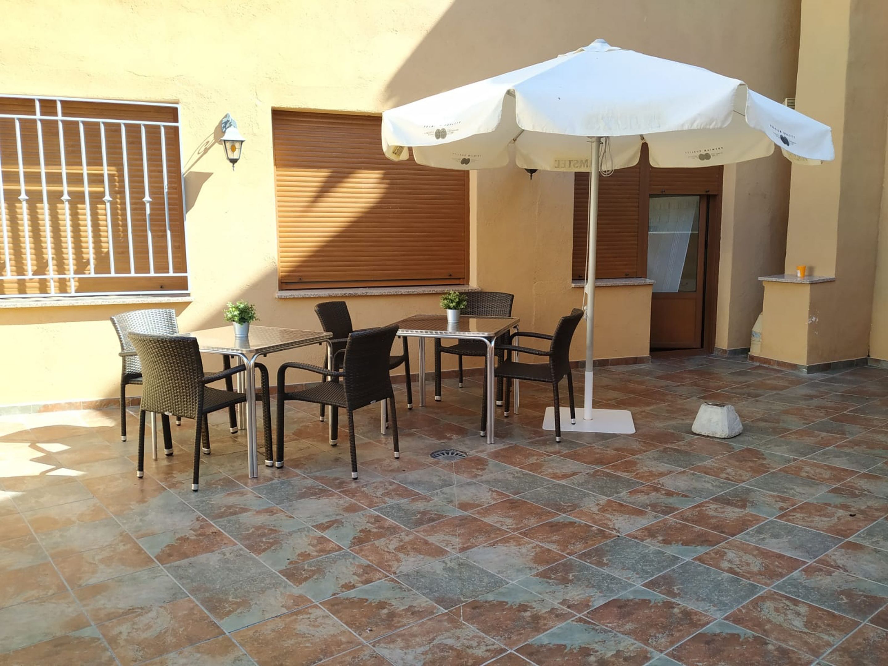An outdoor patio with a table and chairs, a white umbrella, and a potted plant.