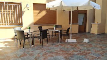 An outdoor patio with a table and chairs, a white umbrella, and a potted plant.