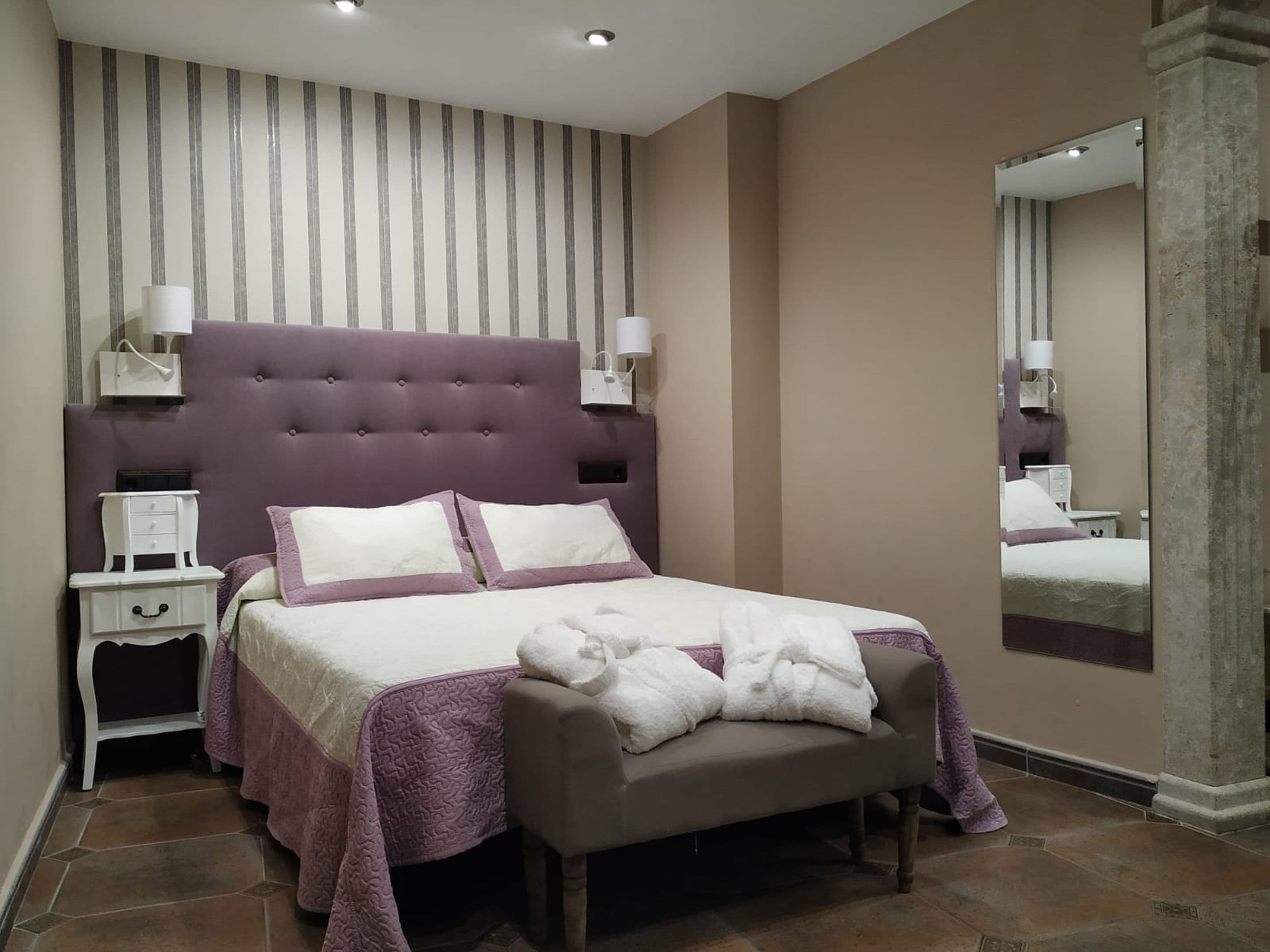 Een slaapkamer met een groot bed, twee nachtkastjes, een spiegel en een hoofdbord.