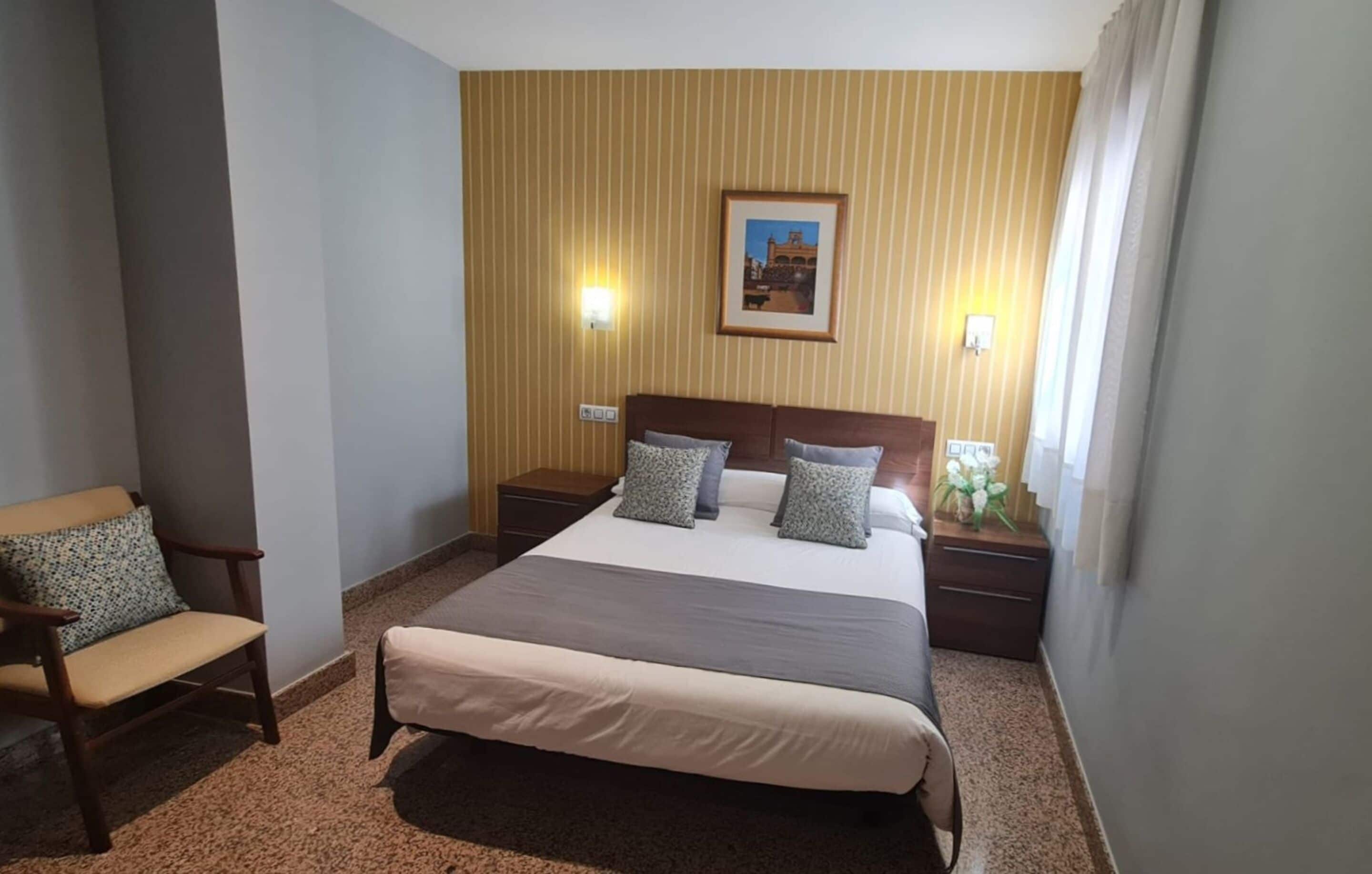 Habitación de hotel con una cama grande, dos mesitas de noche, una silla y un cuadro en la pared.