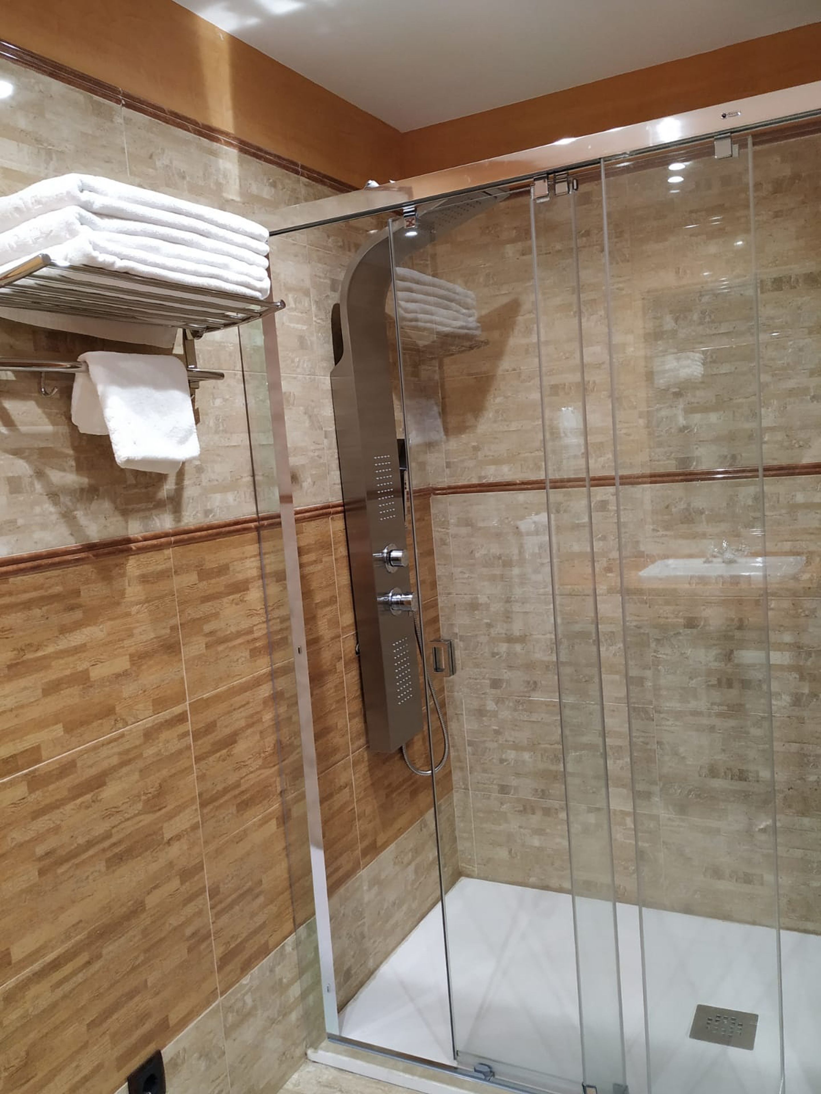 A modern shower with a glass door, a towel rack with folded towels, and a shower control panel.