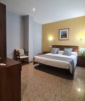 A hotel room with a large bed, a wooden desk, a chair, and a wall-mounted picture.