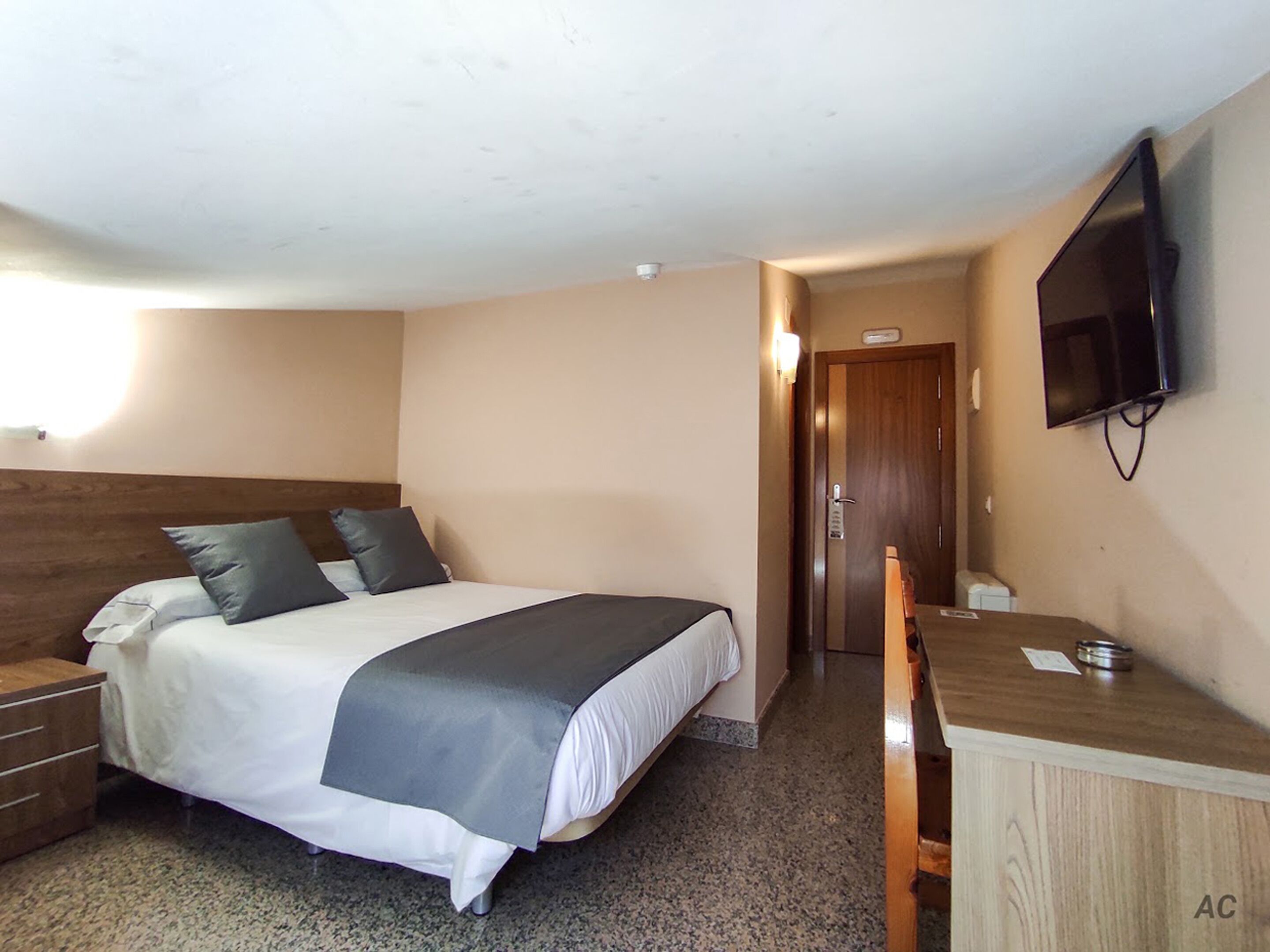 A hotel room with a bed, a desk, a chair, a television, and a door.