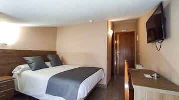 Habitación de hotel con cama, escritorio, silla, televisión y puerta.