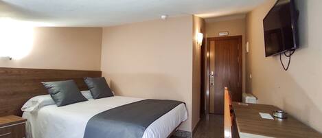 A hotel room with a bed, a desk, a chair, a television, and a door.