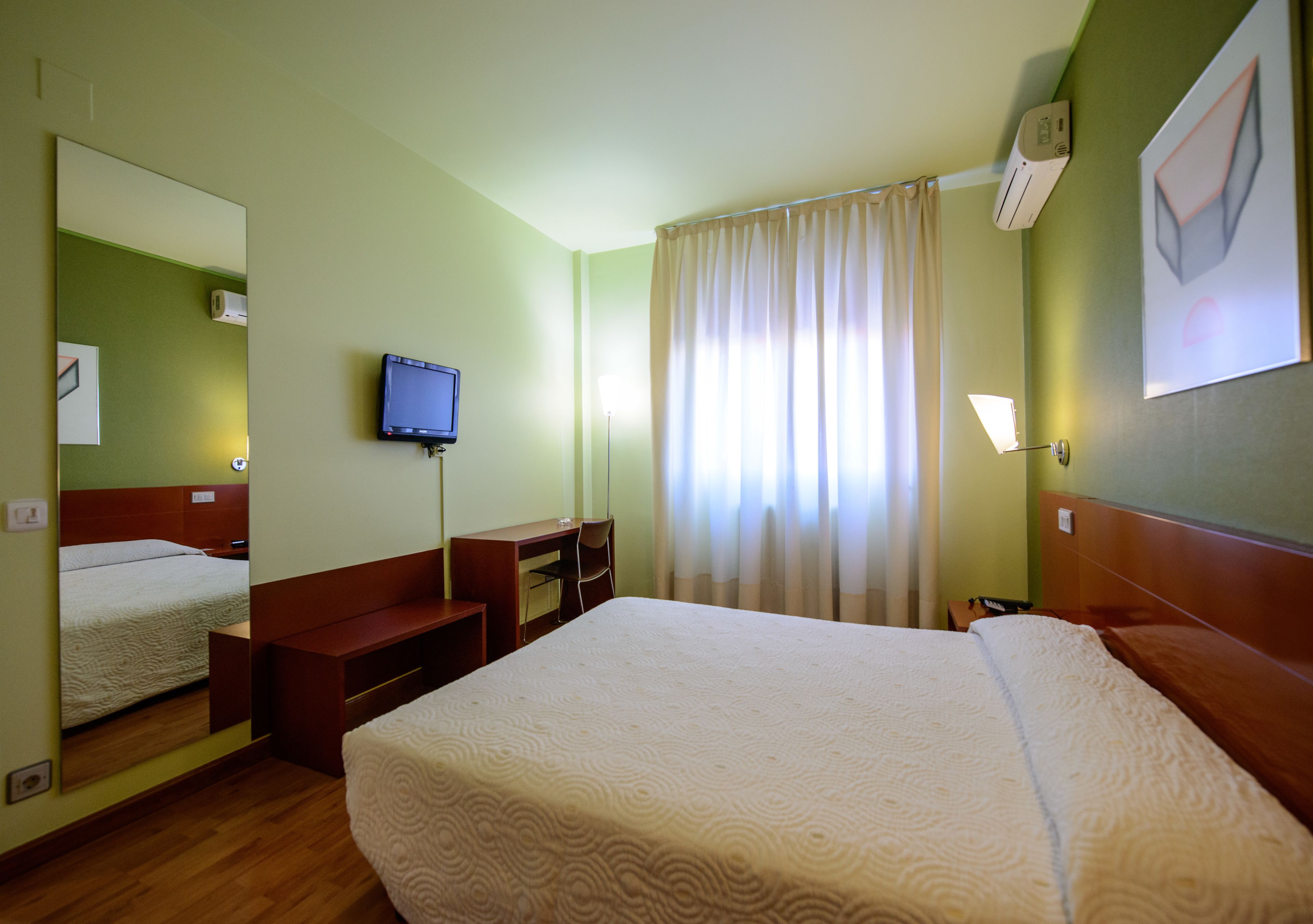 Una habitación de hotel con una cama grande, un escritorio, una silla, un televisor y una ventana con cortinas.