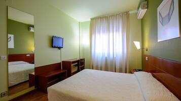Una habitación de hotel con una cama grande, un escritorio, una silla, un televisor y una ventana con cortinas.