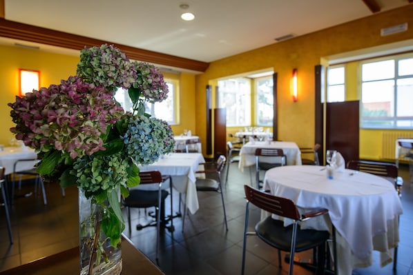Ein Restaurantinnenraum mit runden Tischen, Stühlen und einem Blumenstrauß auf einem Tisch.