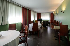 A hotel dining area with round tables, wooden chairs, and a television in the center. - El Paso Honroso (Hospital de Orbigo)