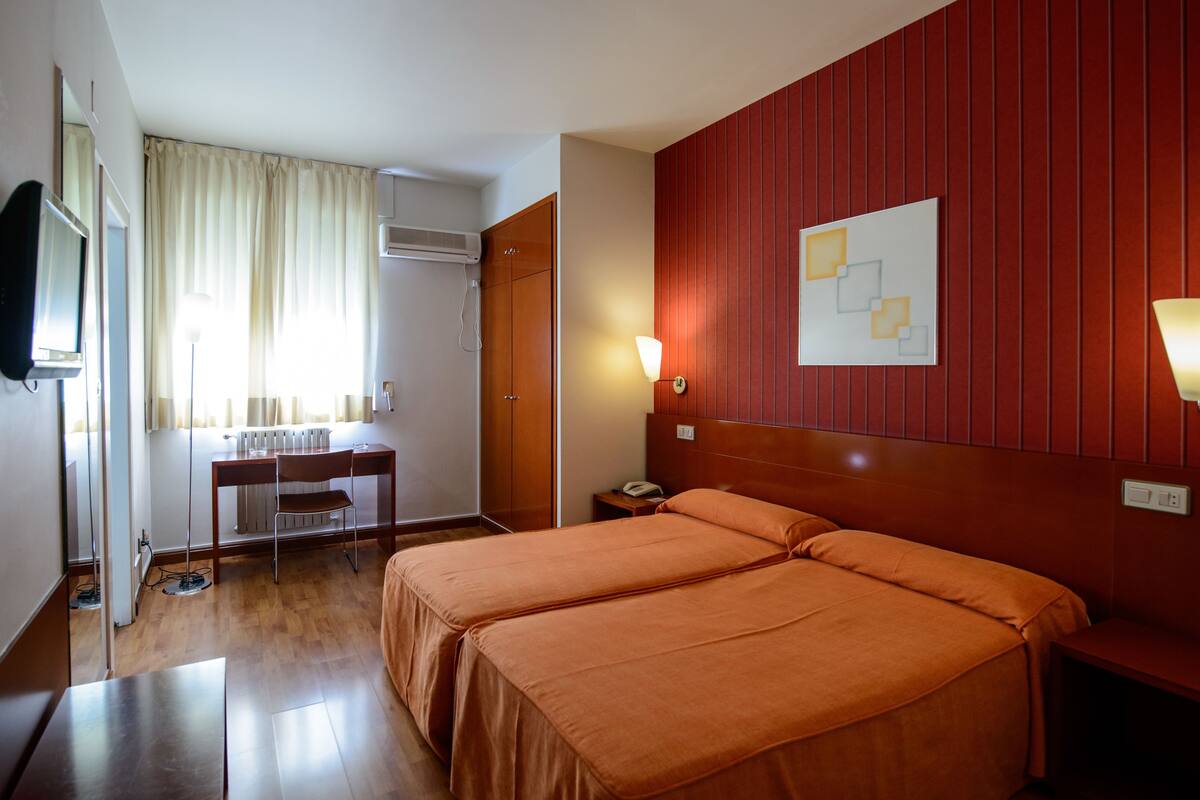 Habitación de hotel con dos camas, un escritorio, una silla, un televisor y una obra de arte colgada en la pared.
