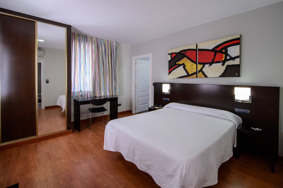 Una habitación de hotel con una cama grande, un escritorio, una silla, un armario y un cuadro en la pared.