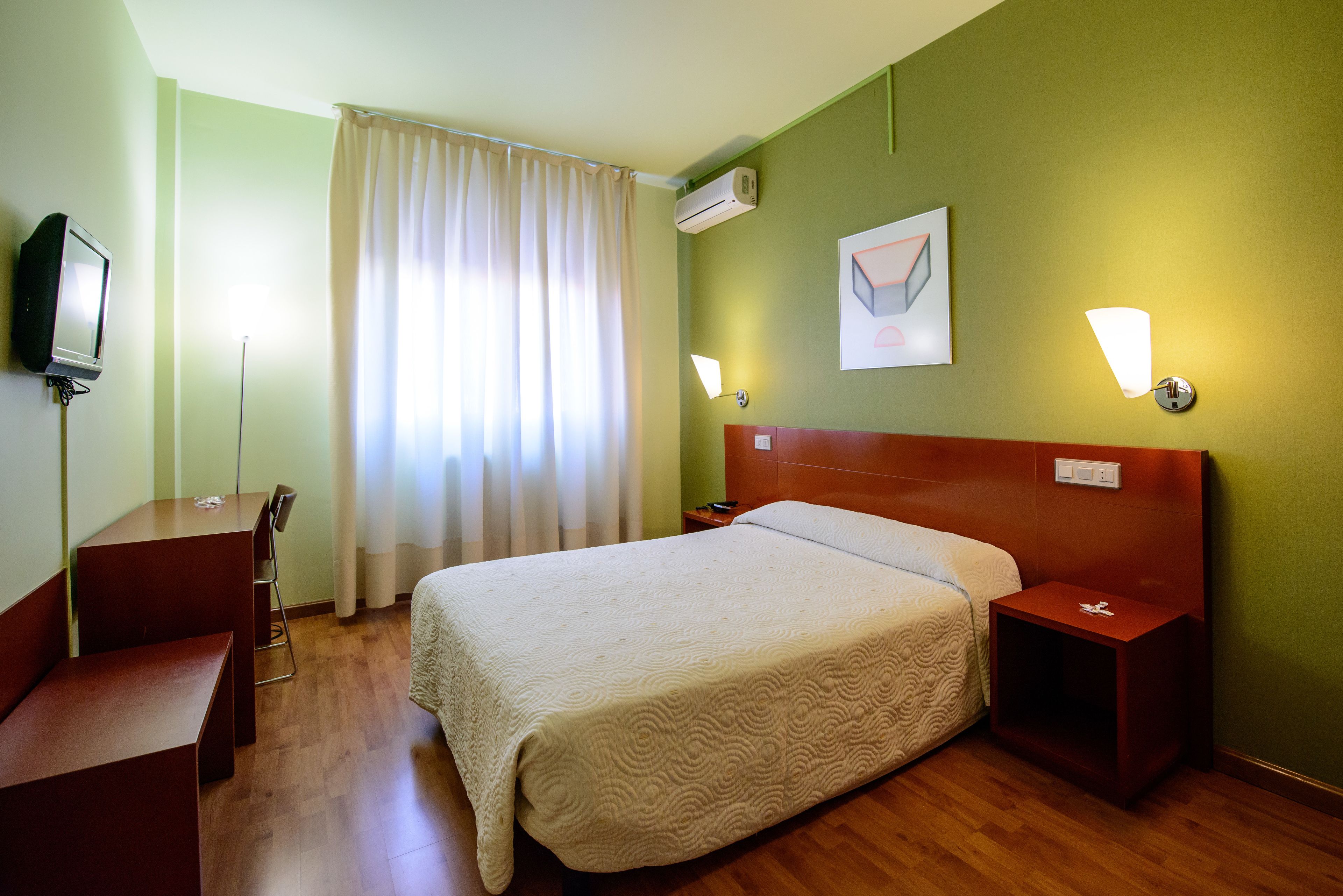 Una habitación de hotel con cama, escritorio, silla, televisor y mesita de noche.