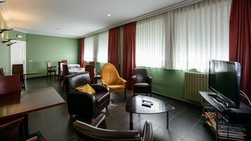 A hotel room with a living area featuring leather sofas, a coffee table, a TV, and a dining area with a table and chairs.