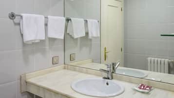Un baño con lavamanos blanco, espejo y toallero con varias toallas blancas.