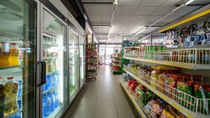 A grocery store aisle with refrigerated sections on the left and shelves stocked with snacks on the right. - El Paso Honroso (Hospital de Orbigo)