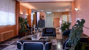 A hotel lobby with a check-in counter, seating area, and a staircase leading to the upper floors. - El Paso Honroso (Hospital de Orbigo)