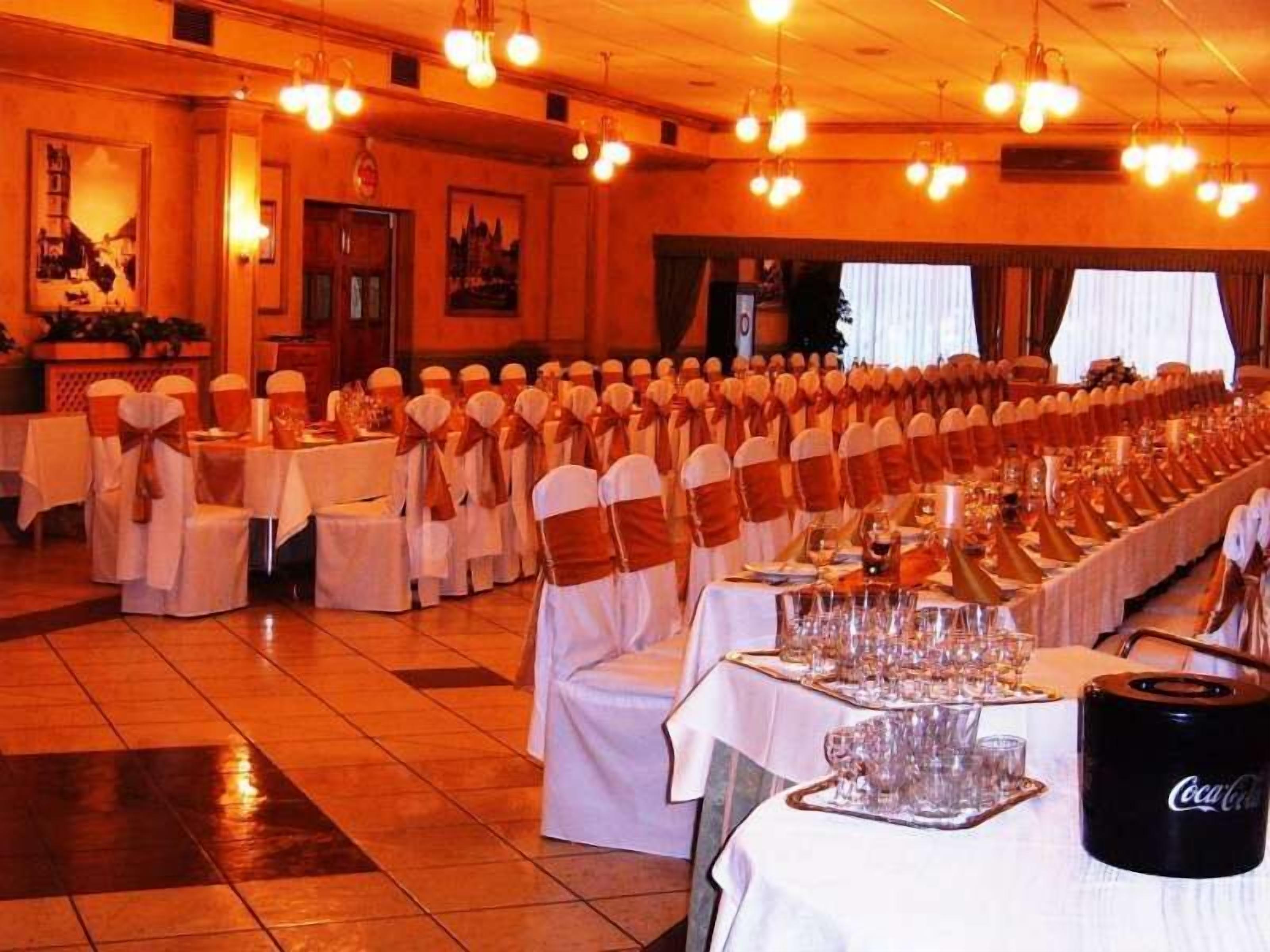 A banquet hall with rows of tables set for a formal event, adorned with white tablecloths and chairs with orange sashes.
