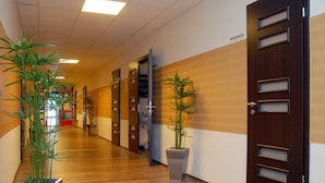 A hallway with wooden flooring, a reception desk, and two potted plants. - Sport Hotel (Debrecen)