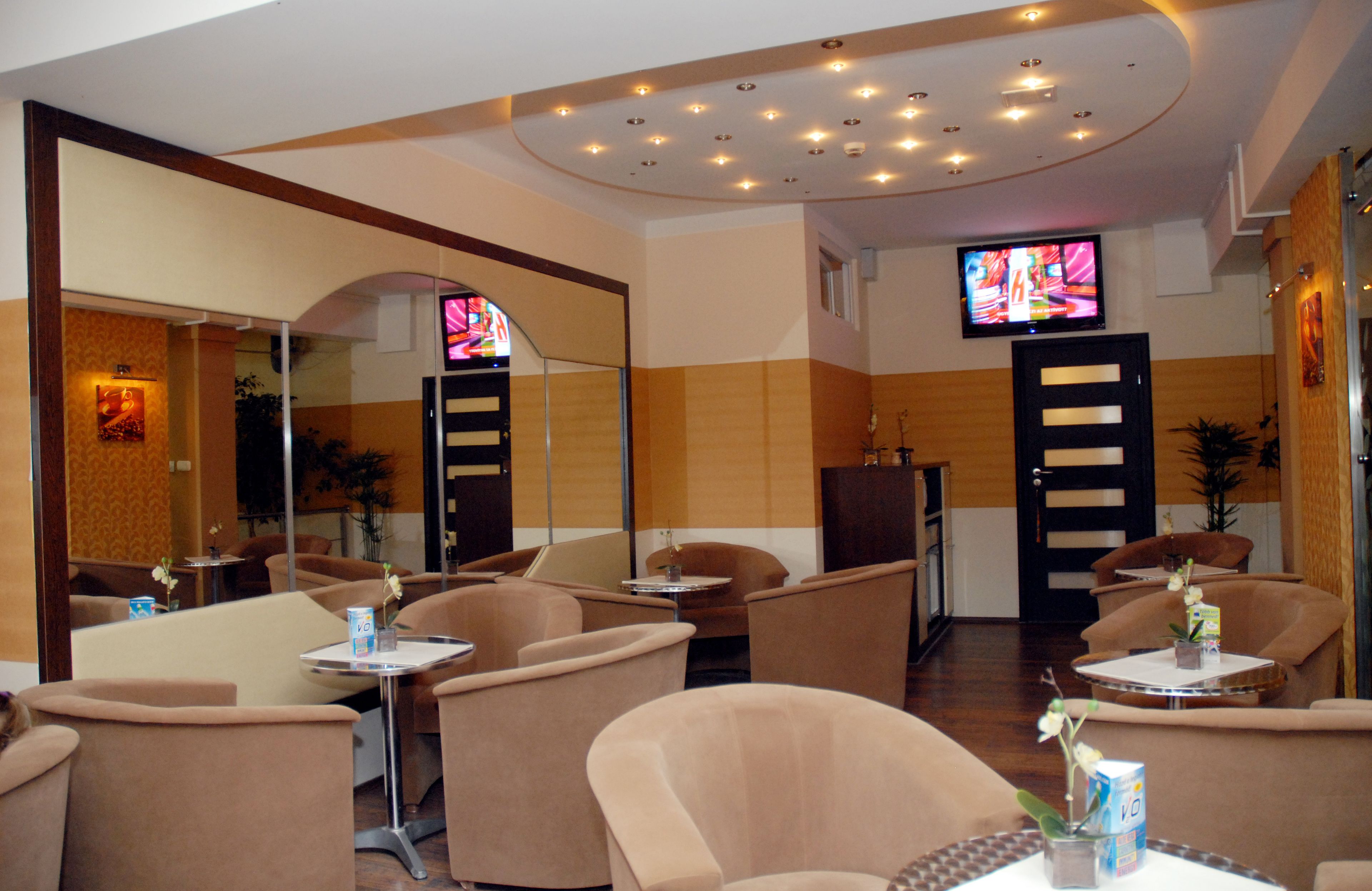 A hotel lobby with multiple seating areas, a television mounted on the wall, and a mirror reflecting the space.