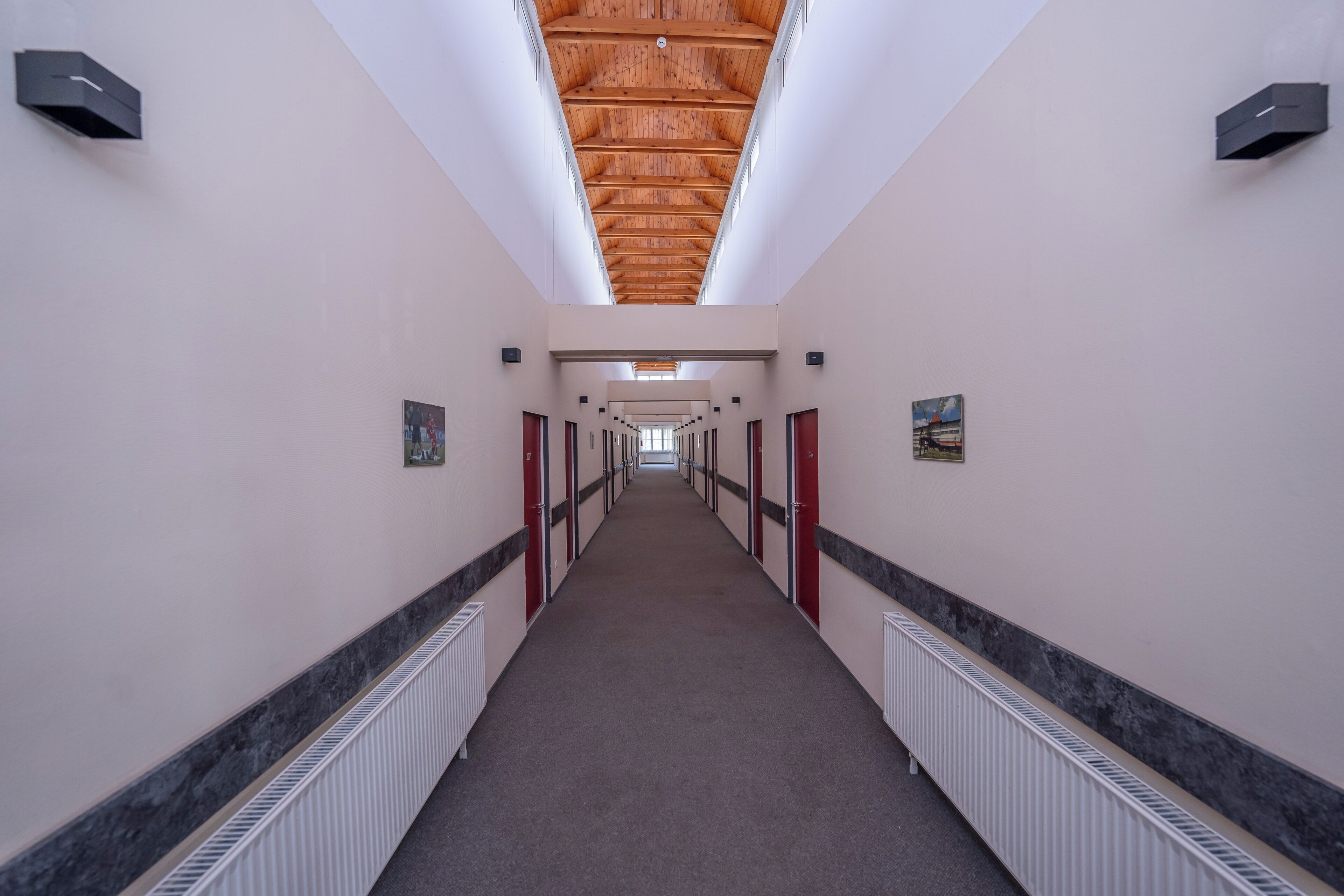 A long, narrow hallway with a wooden ceiling, white walls, and red doors.