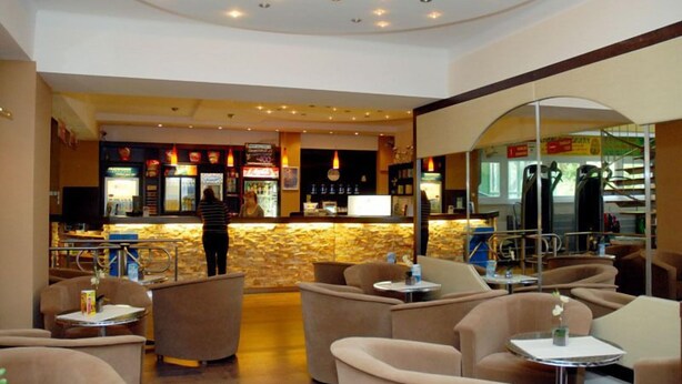 A hotel lobby with a bar area, seating arrangements, and a staircase leading to an upper level. - Sport Hotel (Debrecen)