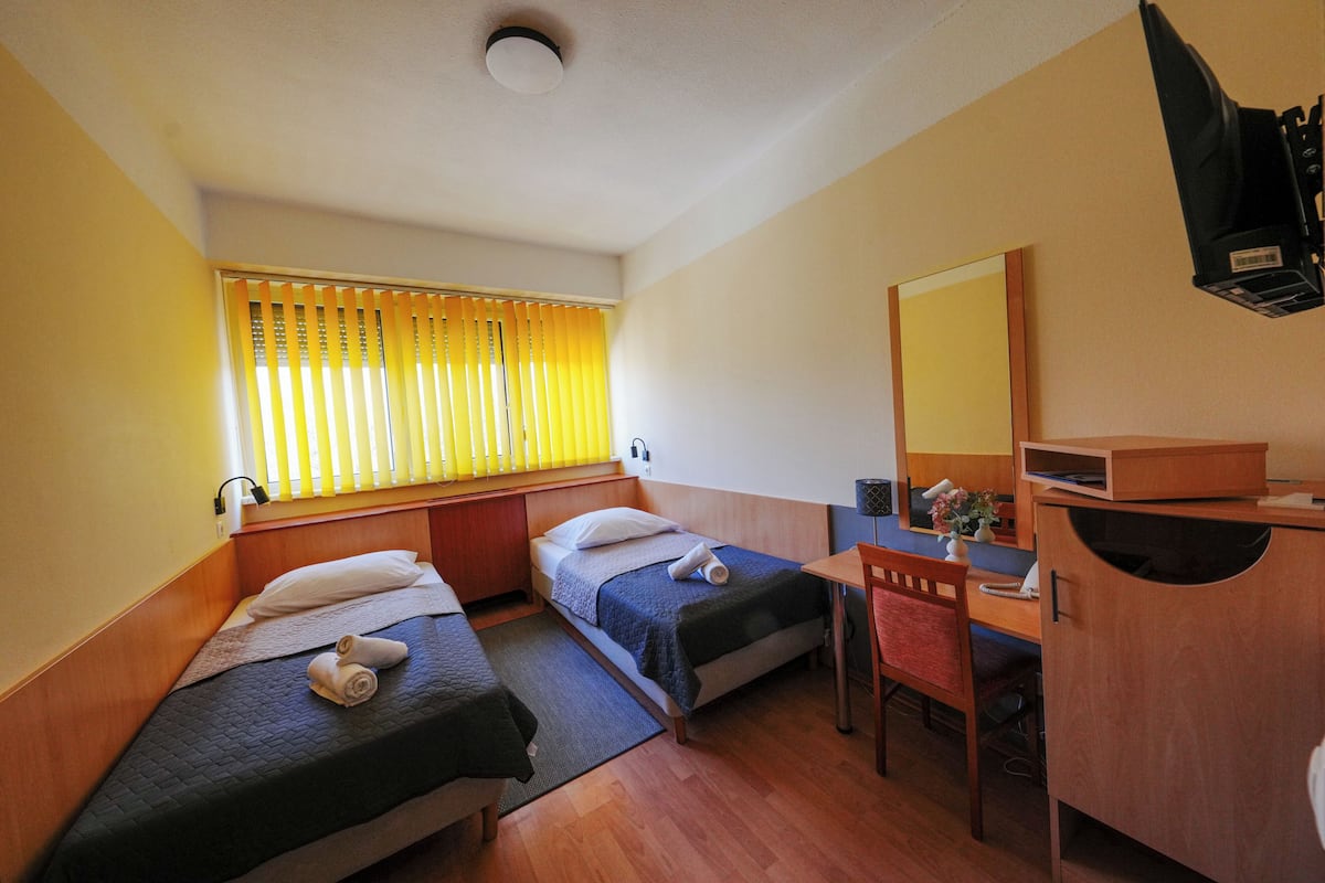 A hotel room with two beds, a desk, a chair, a mirror, and a window with blinds.
