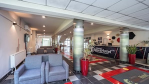 A hotel lobby with a reception desk, seating area, and a check-in counter. - Sport Hotel (Debrecen)