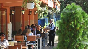 An outdoor cafe with tables and chairs, a waiter serving a customer, and a Coca-Cola sign. - Sport Hotel (Debrecen)