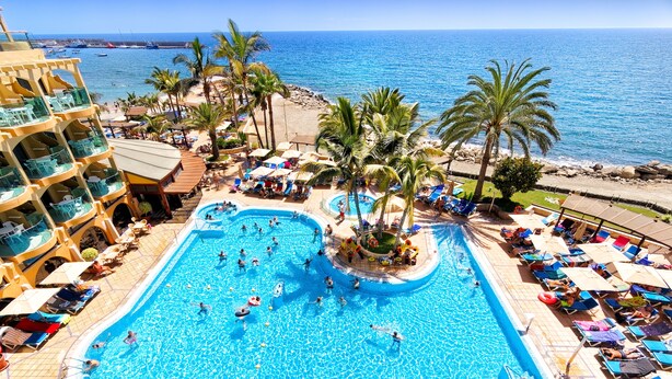 Ein Resort mit großem Pool, Palmen und Blick auf den Ozean.