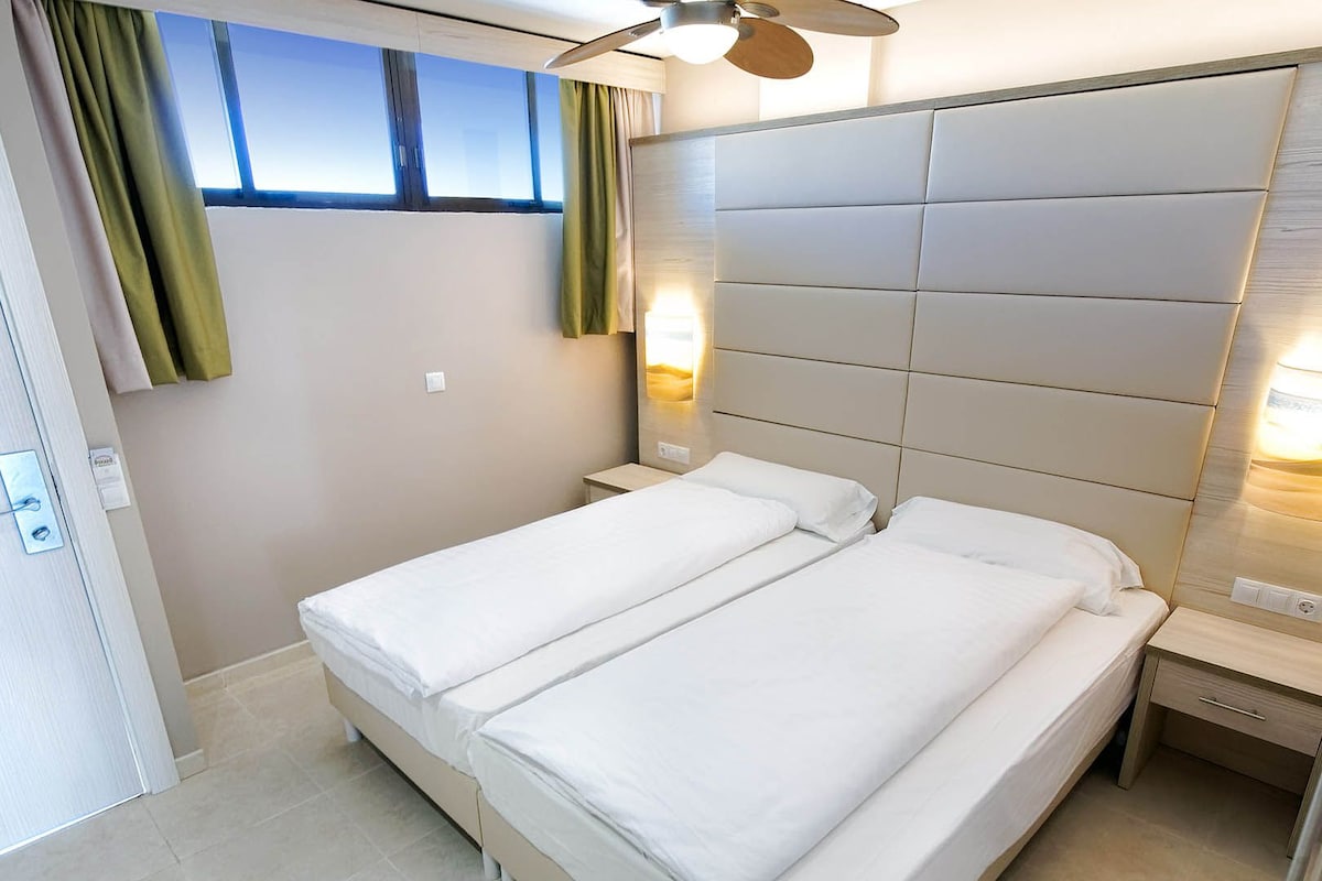 A hotel room with a bed, a nightstand, a wall-mounted light, and a ceiling fan.