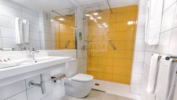 Un baño moderno con lavamanos, espejo y retrete blancos, y una ducha con azulejos amarillos.