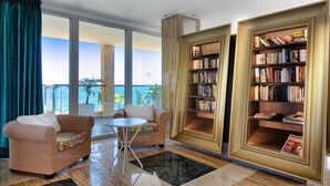 Ein geräumiger Wohnbereich mit Balkon und Meerblick, möbliert mit Korbstühlen und einem kleinen Tisch.