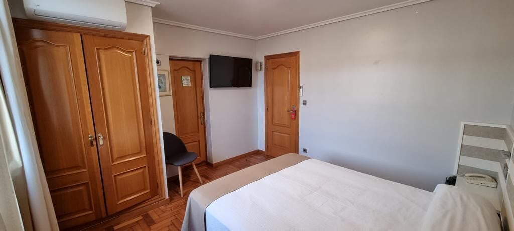 Un dormitorio con cama, una silla, televisión y armarios de madera.