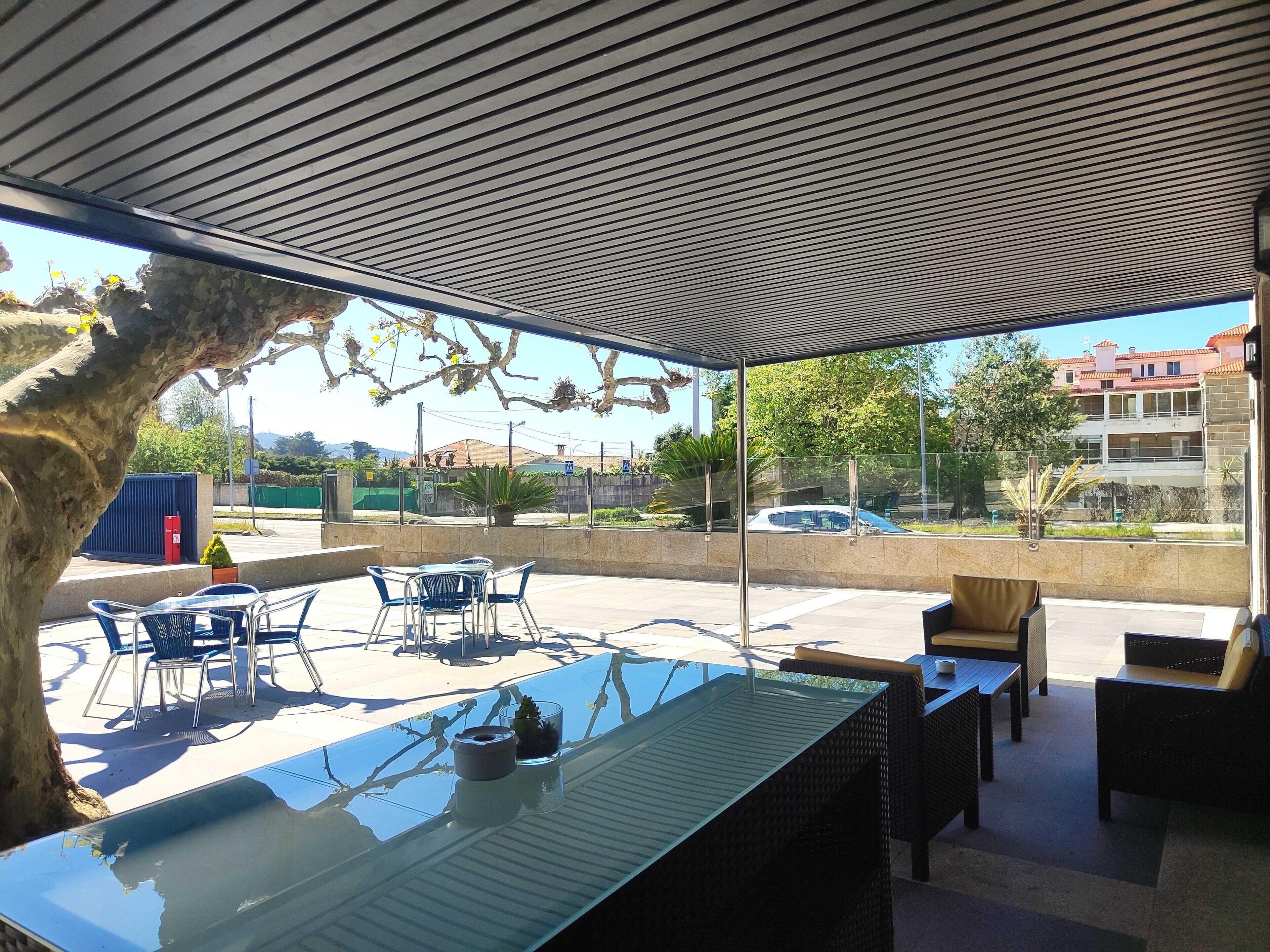 Un patio al aire libre con una mesa de vidrio, sillas y mobiliario de mimbre.