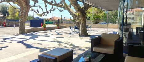 An outdoor seating area with tables and chairs, a covered section, and trees.