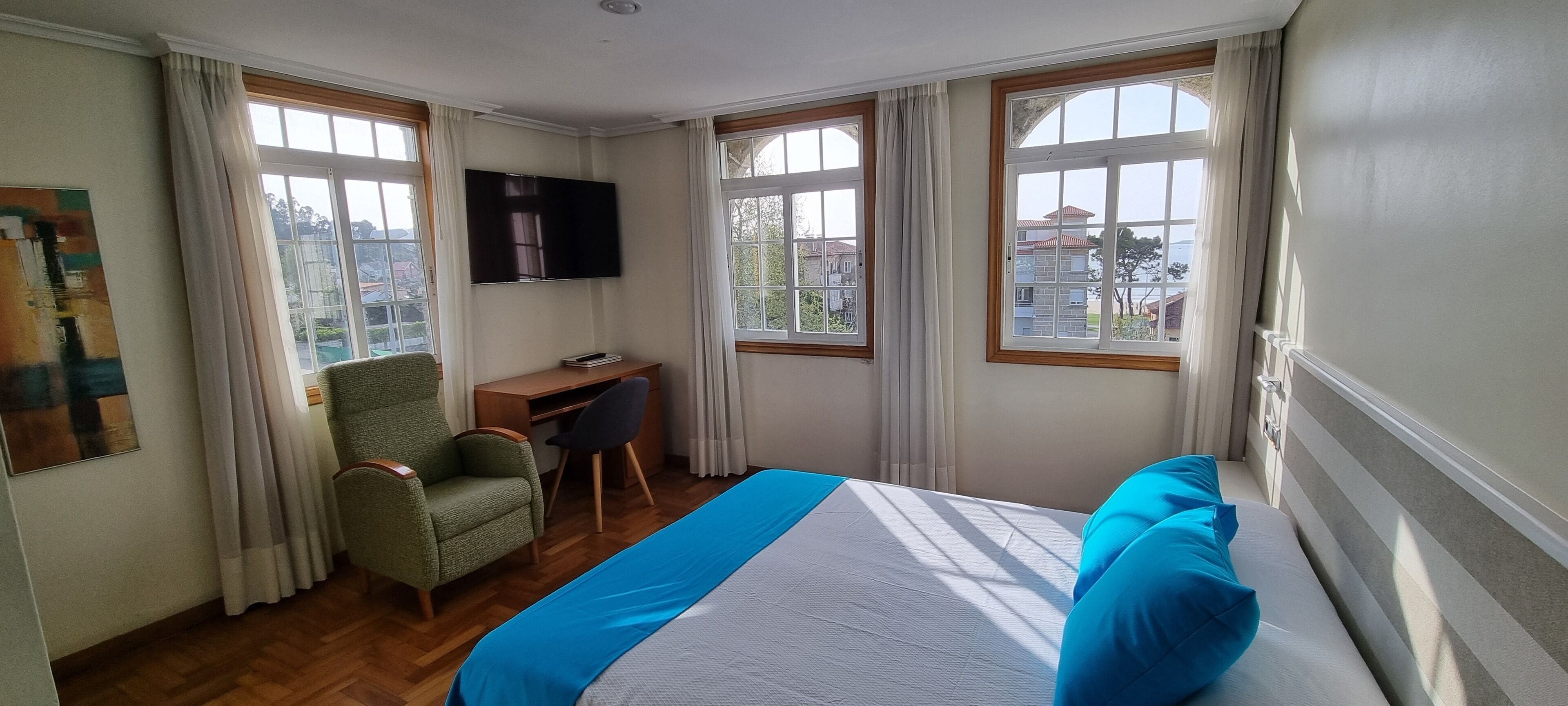 Ein Hotelzimmer mit Bett, Schreibtisch, Stuhl, Fernseher und großen Fenstern.