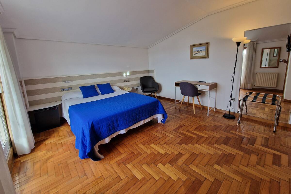 A hotel room with a bed, a desk, a chair, and a radiator.