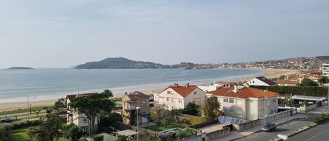 A coastal residential area with houses, a beach, and a hill in the distance.