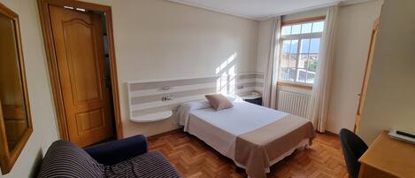 Una habitación de hotel con cama, mesita de noche, silla, escritorio y ventana con vistas.