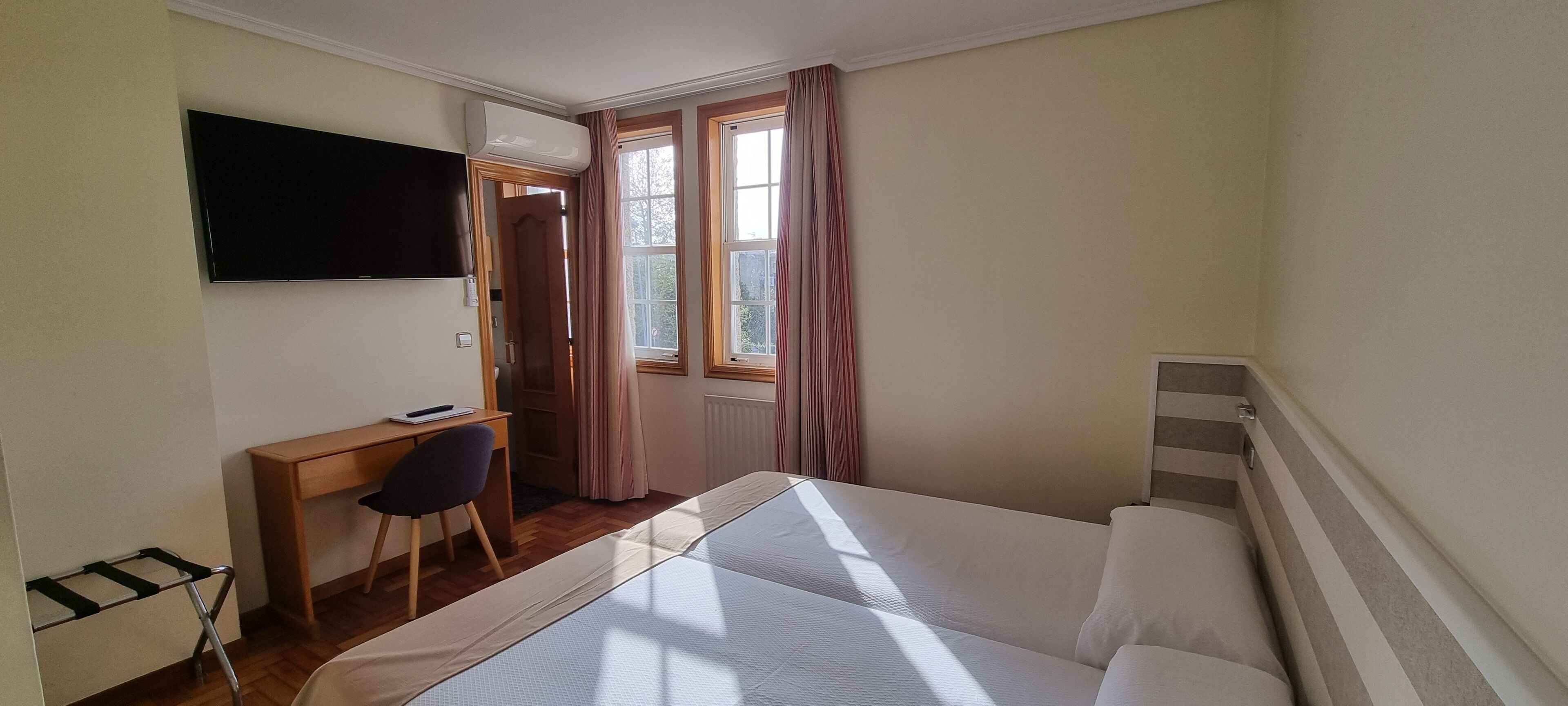 Una habitación de hotel con cama, escritorio, silla, televisión y ventana con cortinas.