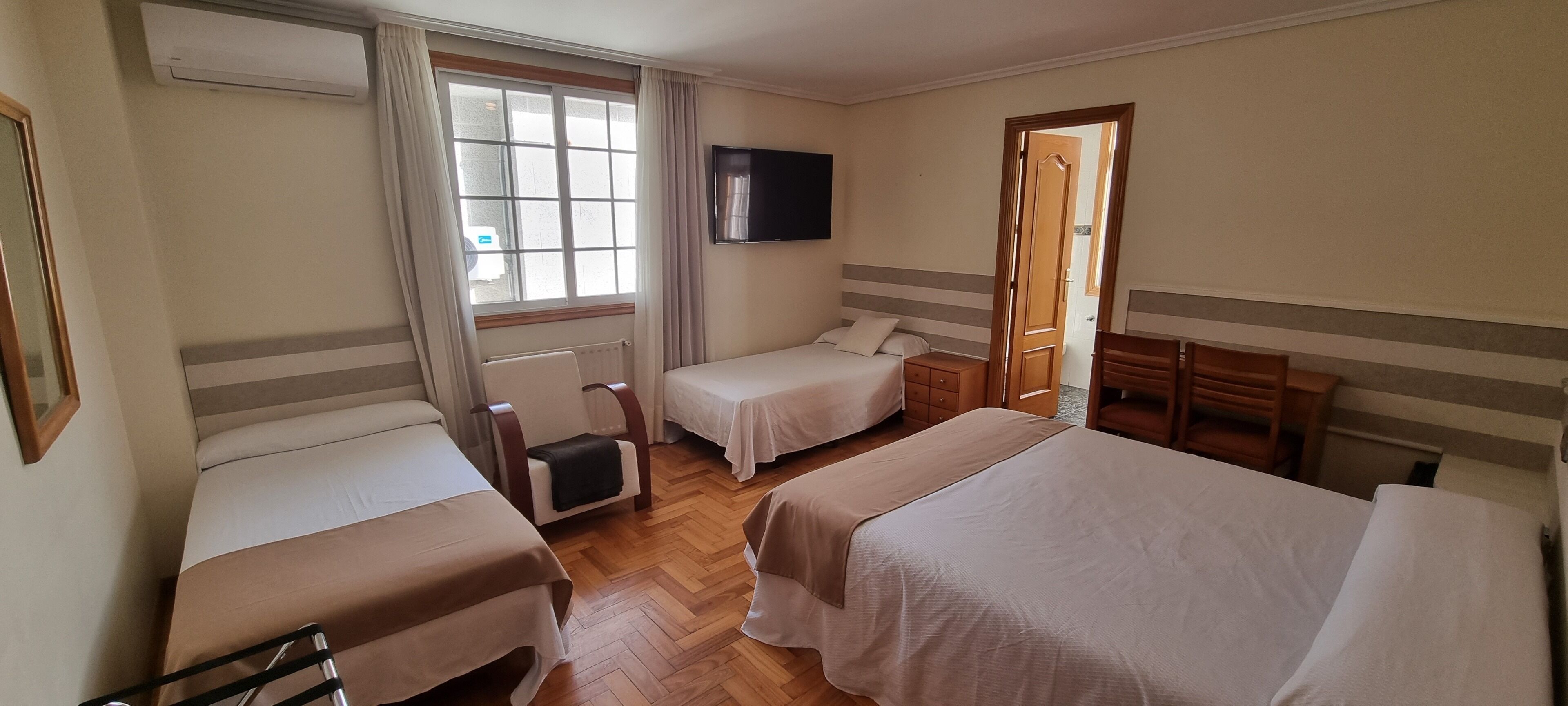 Ein Hotelzimmer mit zwei Einzelbetten, einem Holzstuhl, einem Schreibtisch mit Stuhl und einem an der Wand montierten Fernseher.