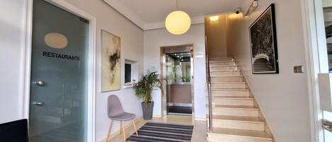 A modern interior with a staircase, a reception desk, and a door labeled "RESTAURANTE".