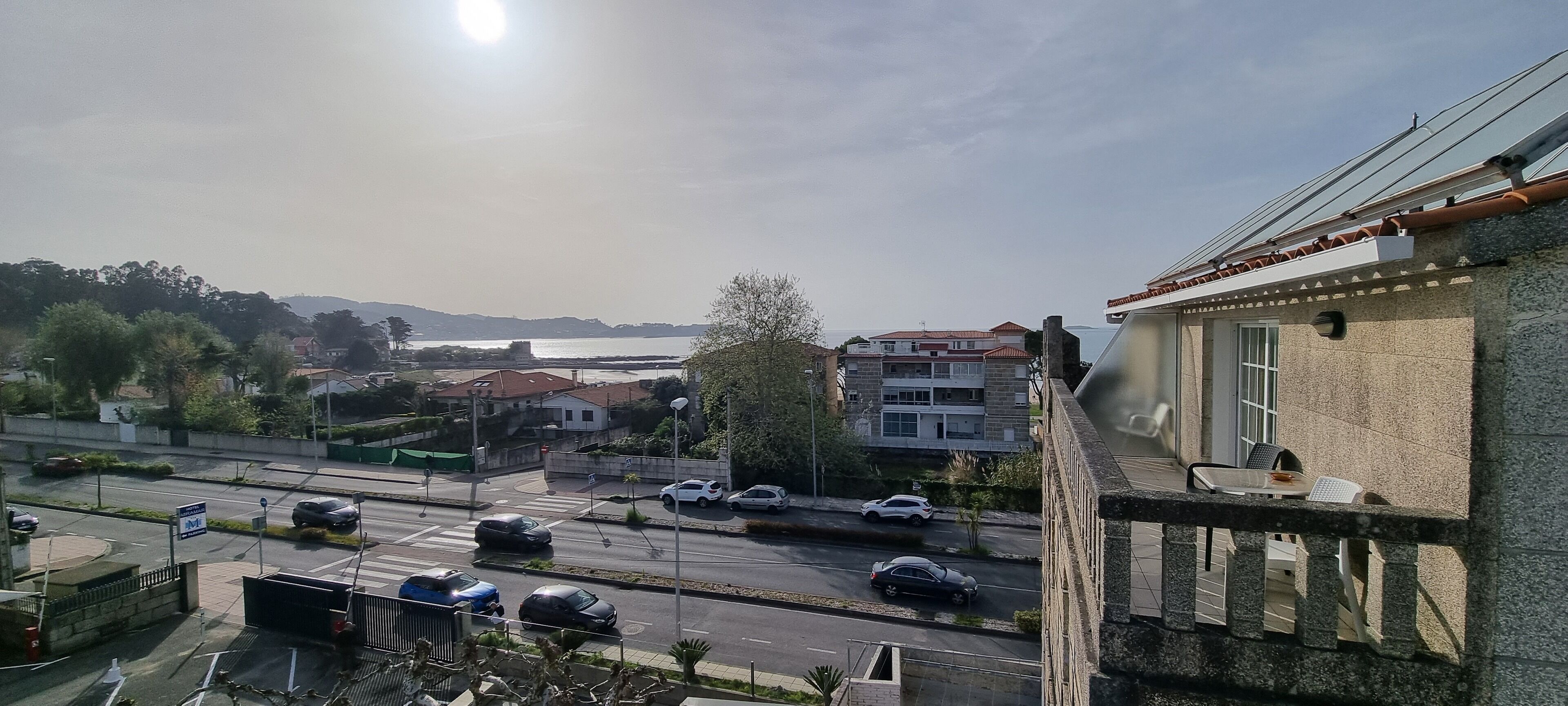 Vista de una carretera costera con coches, un puente y edificios al fondo.