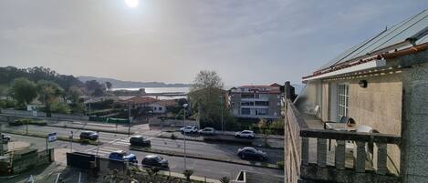 Vista de una carretera costera con coches, un puente y edificios al fondo.