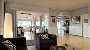 Un amplio vestíbulo de hotel con zona de comedor, mostrador de recepción y cocina al fondo.