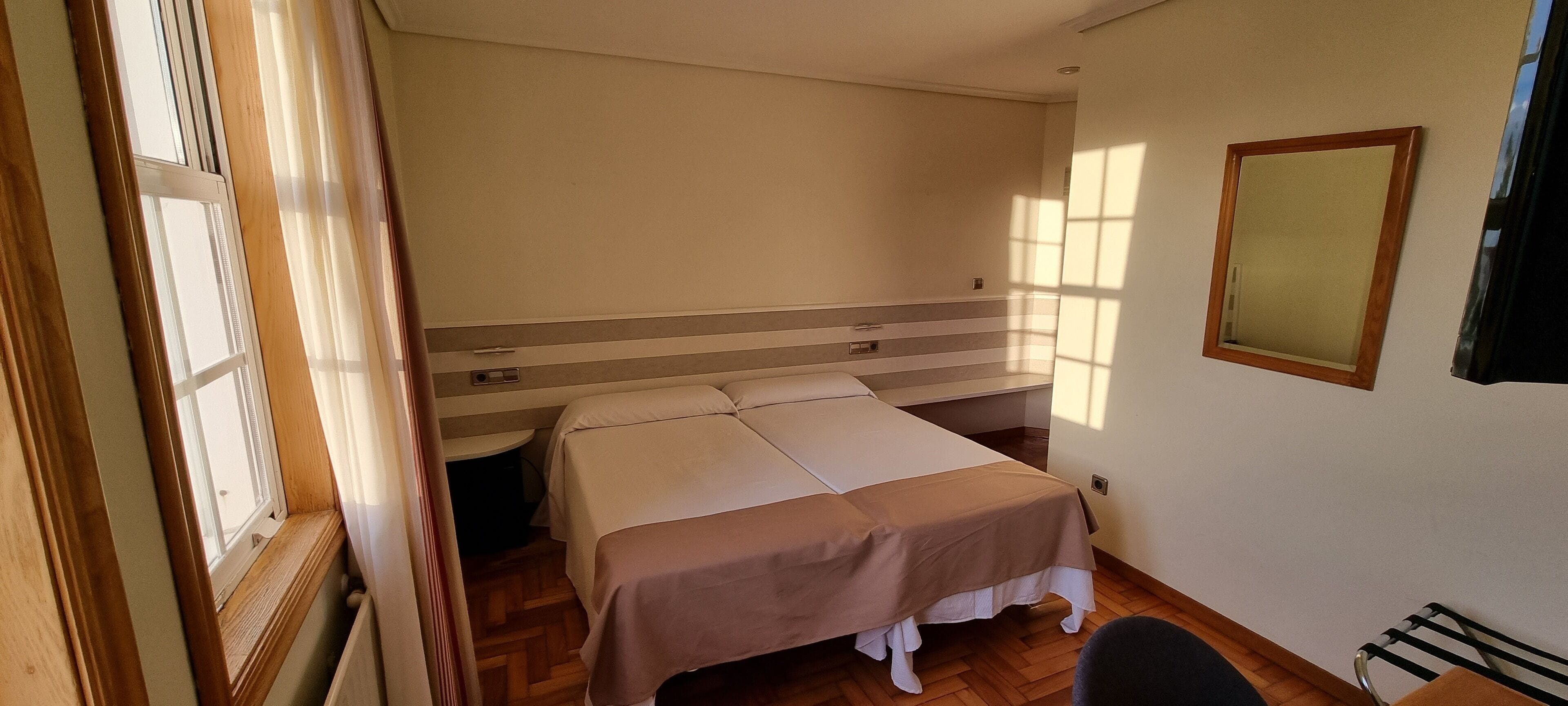 A bedroom with a bed, a bedside table, a mirror, and a window with blinds.