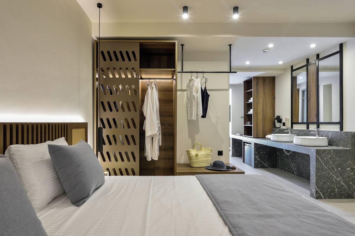 Een moderne hotelkamer met een groot bed, een badkamer met een marmeren wastafel en een houten garderobe.