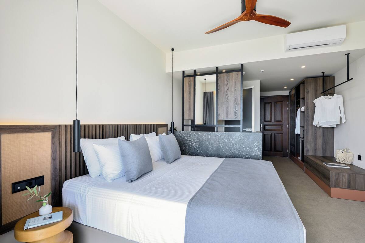 Een moderne hotelkamer met een groot bed, een houten hoofdbord, een nachtkastje met een plant en een plafondventilator.