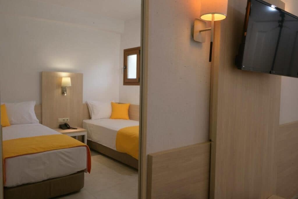 Habitación de hotel con dos camas, televisión, mesita de noche y lámpara.